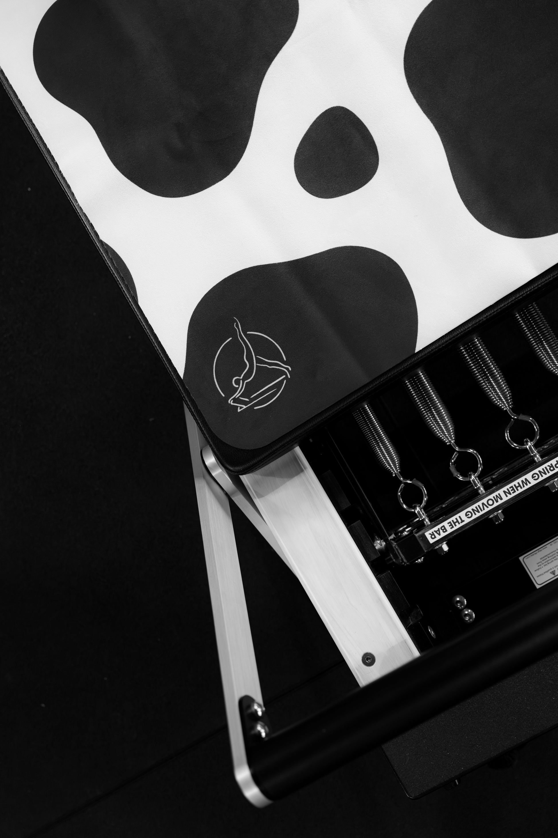 Black and white image of a reformer mat with a cow print design on the body.